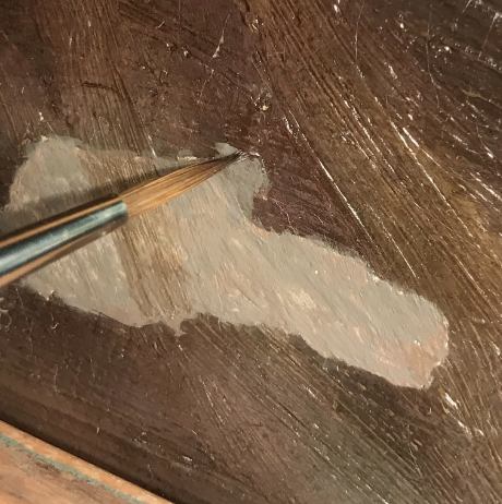 A paintbrush is being used to retouch an oil painting