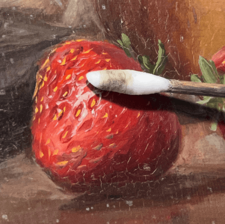 A close up painted strawberry is being cleaned by cotton swab
