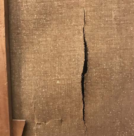 A tear in the canvas of a painting, as viewed from the reverse